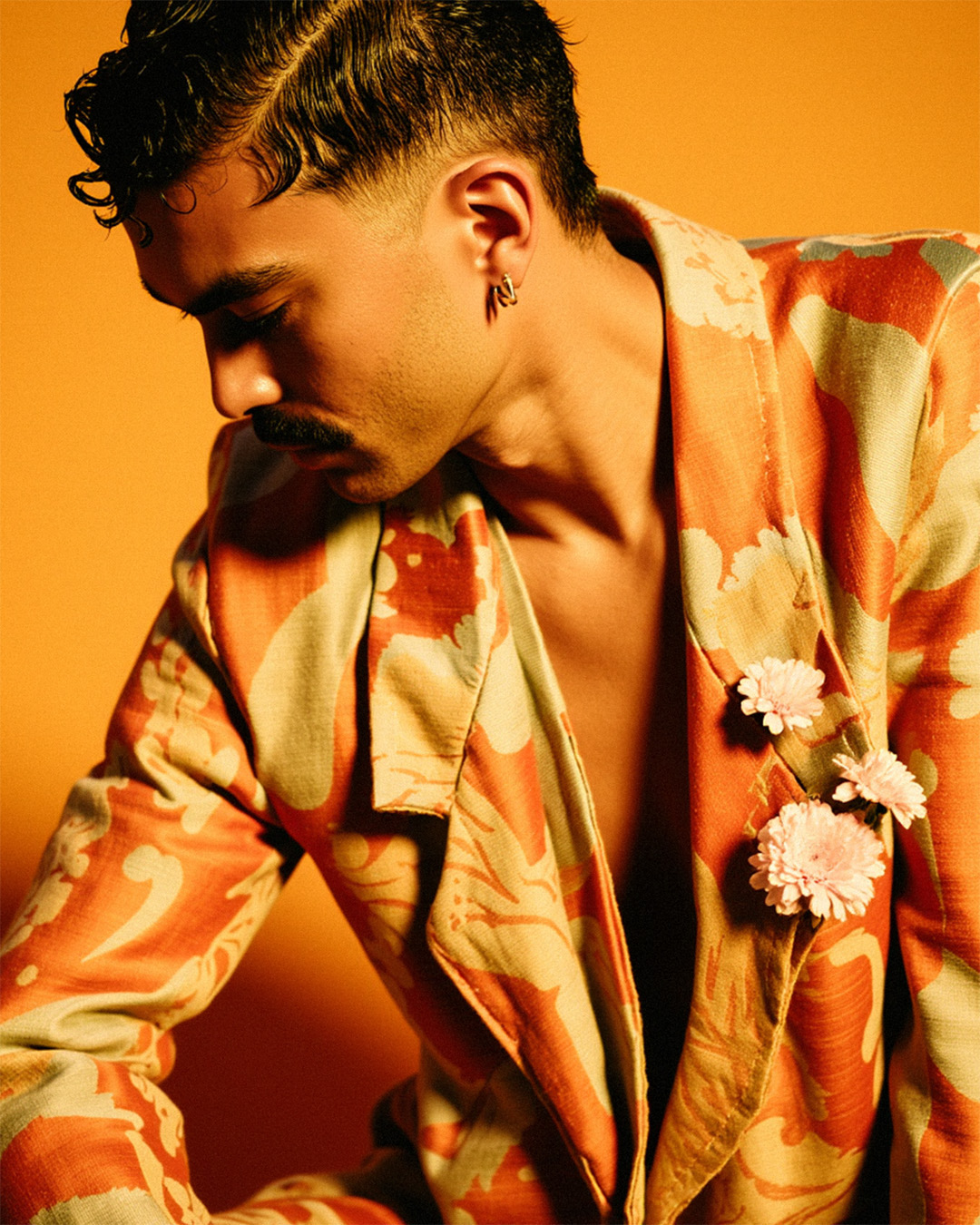 Vestindo um blazer laranja com estampas sutis, Marco Vincit exibe uma composição sofisticada e poética, combinando moda e arte visual. — Laranja, Marco Vincit