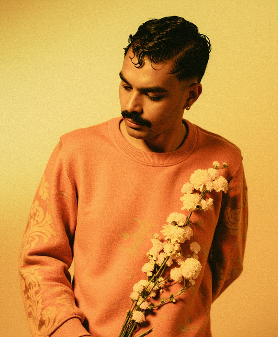 Com um moletom bordado laranja e flores aplicadas ao peito, Marco Vincit une moda e natureza em uma fotografia artística e sofisticada. — Laranja, Marco Vincit