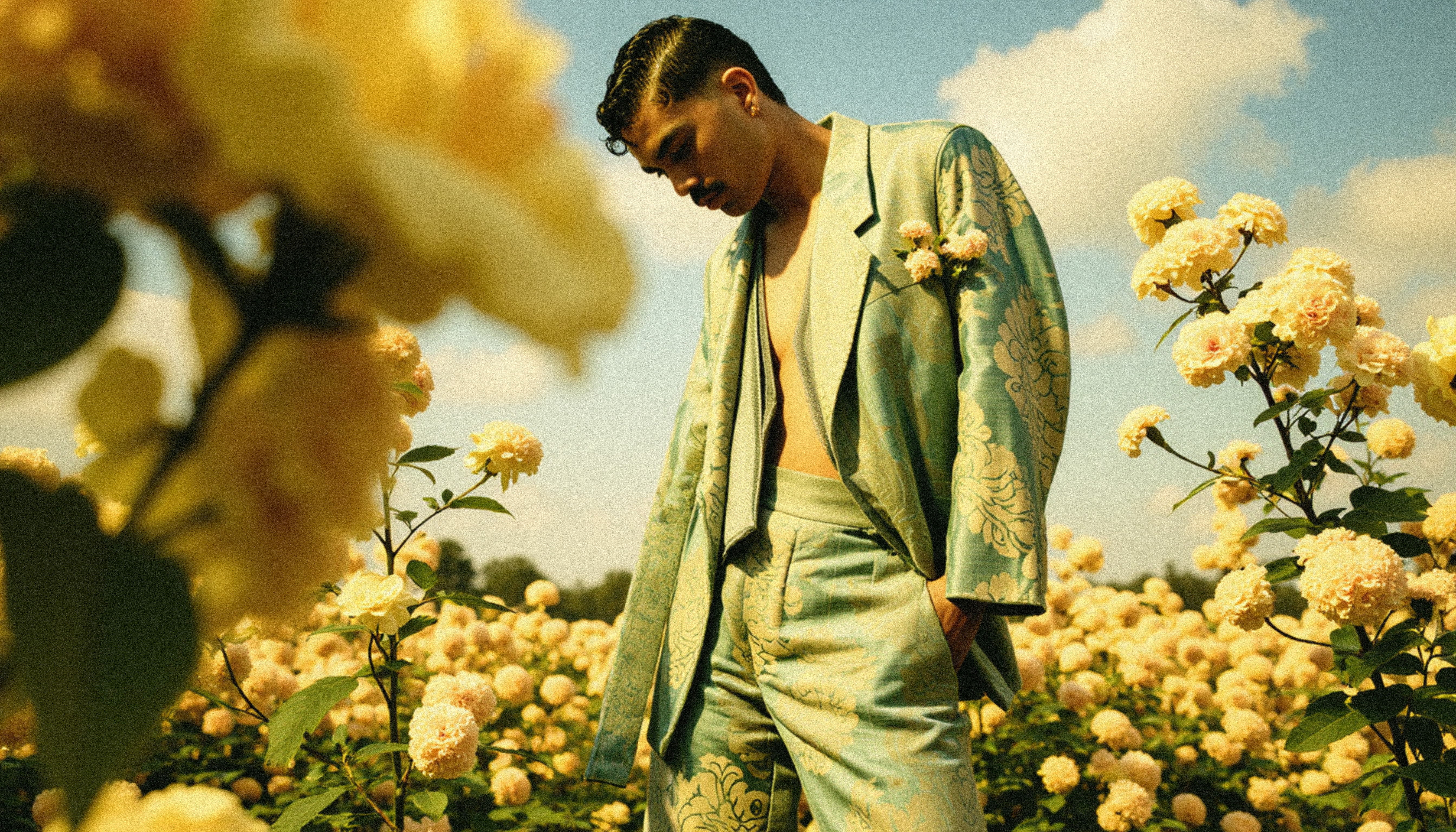 Marco Vincit veste um elegante terno azul em meio a um campo de flores amarelas. A composição harmoniosa entre moda e natureza transmite leveza e sofisticação. — Retratos, Marco Vincit